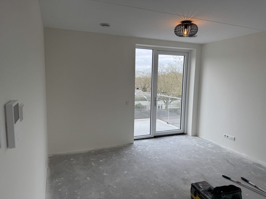 Pas opgeleverde kamer in een appartement met balkondeuren en kale wanden, klaar voor het vlies